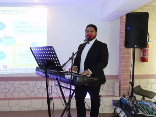 Homme en costume jouant du piano avec un microphone devant une présentation en arrière-plan.