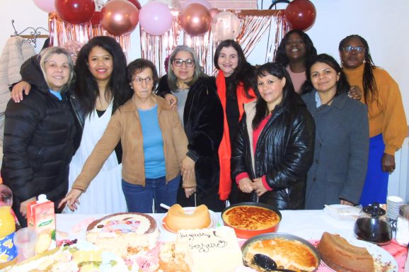 Groupe de femmes souriantes devant une table de fête avec des gâteaux et des décorations.